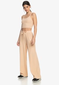 Beige ribbed crop top and wide-leg pants with drawstring waist. Features a small logo detail on the top and textured fabric.