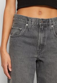 Hög midja, grå denimjeans med en klassisk femfickorsdesign, synlig sömnad och metallfästen på midjebandet.