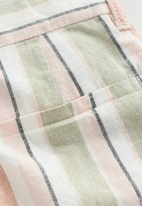 Gros plan sur un tissu à rayures verticales en rose pâle, beige, blanc et noir, avec une poche cousue et des détails de couture.