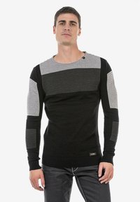 Schwarzer und grauer gerippter Pullover mit Rundhalsausschnitt und langen Ärmeln, der strukturierte Akzente an den Schultern und Ärmeln aufweist.