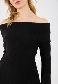 Vestido negro de canalé con escote asimétrico, mangas largas, tejido texturizado y silueta ajustada. Diseño simple y moderno.