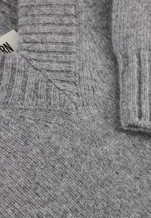 Close-up of a gray knitted sweater showing ribbed collar, folded detail, and a partially visible white clothing label.