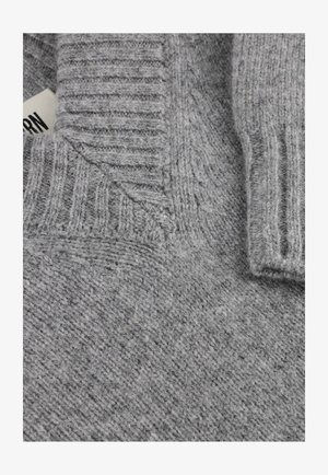 Close-up of a gray knitted sweater showing ribbed collar, folded detail, and a partially visible white clothing label.