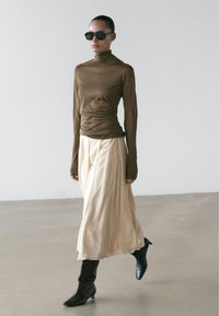 Bruin lang mouw turtleneck top, crèmekleurige vloeiende rok en zwarte enkellaarsjes met puntige neus. Gladde texturen, minimalistisch ontwerp, neutraal kleurenpalet.