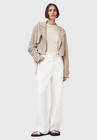Beige Wildleder-Cropped-Jacke, hellgrünes T-Shirt, weiße hochtaillierte weite Hose, schwarze Sandalen mit silbernen Akzenten.