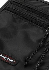 Borsa nera in nylon con più tasche orizzontali, superficie texturizzata e chiusura con cordoncino. Logo Eastpak in evidenza.
