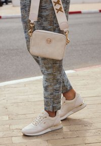 Bílé tenisky s texturovanými detaily a zlatými prvky, zkombinované se vzorovanými modro-bežovými kalhotami a smetanovou crossbody kabelkou.