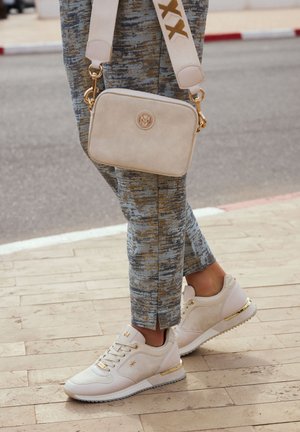 Sneakers bianchi con dettagli testurizzati e hardware dorato, abbinate a pantaloni blu e beige a fantasia e una borsa a tracolla crema.