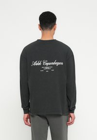 Maglietta a maniche lunghe nera in cotone; presenta la scritta bianca "Arkk Copenhagen" sul retro. Vestibilità rilassata con polsini e orlo a coste.