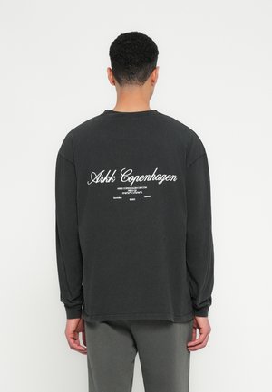 Long-sleeve black t-shirt made of cotton; features white text "Arkk Copenhagen" on the back. Relaxed fit with ribbed cuffs and hem.