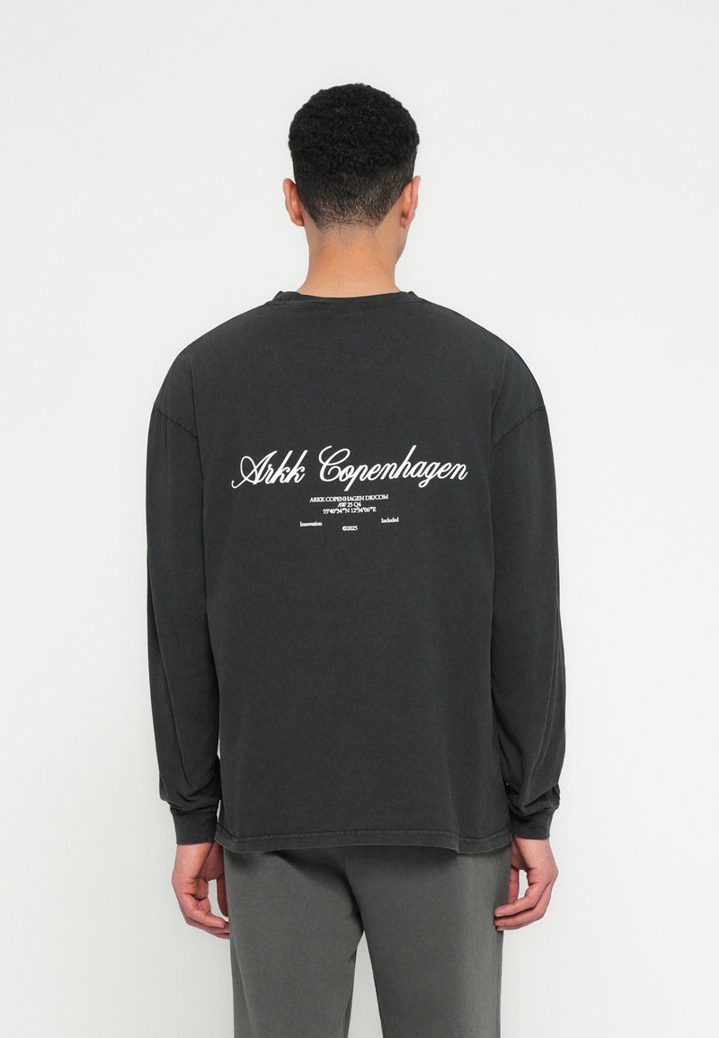 Maglietta a maniche lunghe nera in cotone; presenta la scritta bianca "Arkk Copenhagen" sul retro. Vestibilità rilassata con polsini e orlo a coste.
