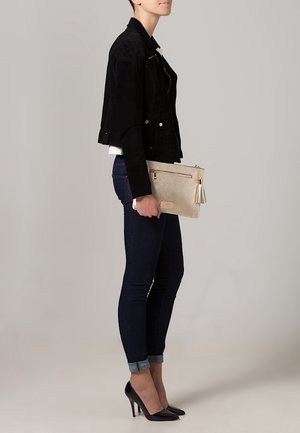 Giacca cropped in suede nera, camicia bianca aderente, jeans scuri e tacchi alti neri. Tiene una clutch beige chiaro con dettaglio a frangia.