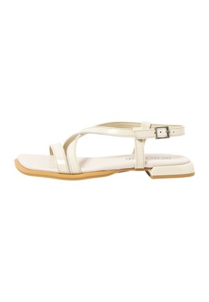 Beige flat sandal with thin crisscross straps, adjustable buckle ankle strap, square toe, and low square heel with light brown sole.
