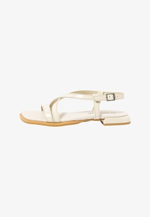 Beige flat sandal with thin crisscross straps, adjustable buckle ankle strap, square toe, and low square heel with light brown sole.