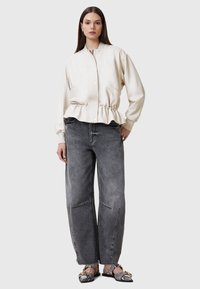 Cremefarvet, blød læderjakke med peplum-talje, parret med falmede, løstsiddende grå jeans og mønstrede sorte slip-on sko.