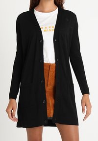 Svart långärmad cardigan med knäppning fram, två framfickor och en enkel design. Lättstickad tyg.