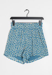 Shorts bleus avec un motif floral composé de marguerites blanches aux centres jaunes. Taille élastique avec plis, coupe décontractée et ourlets latéraux.