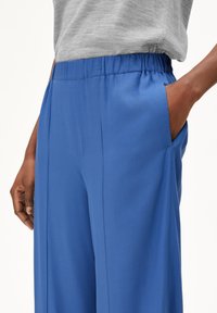 Blue wide-leg trousers with a relaxed fit, featuring an elastic waistband and side pockets. Made from a smooth fabric with a matte finish.