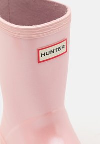 Roza gumijasta škornja za dež, z gladko teksturo in zaobljenim vrhom. Ima črno-rdeči oznako "HUNTER" na strani.