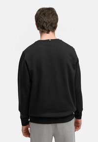 Sudadera negra de manga larga y cuello redondo, con un tejido texturizado y puños acanalados. La parte posterior presenta un diseño sencillo con una etiqueta cerca del escote.