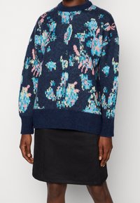Granatowy sweter dzianinowy z kolorowym abstrakcyjnym wzorem w odcieniach niebieskiego i różowego, okrągły dekolt, luźny krój, zestawiony z czarną spódnicą.