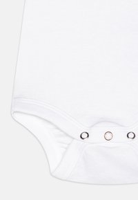 Hvit bomullsdress med trykknapp-feste i bunnen, elastiske kanter for bedre passform og en glatt tekstur.