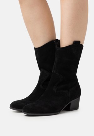 Bottines en daim noir avec un design de couture incurvé et un talon bloc bas. Elles comportent une fermeture éclair latérale et une languette de tirage en boucle à l'arrière.