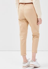 Pantalons beiges au design ajusté, avec des poignets retroussés et une ceinture tressée marron. Associés à des baskets blanches avec un accent gris clair.