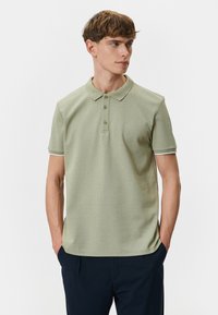Kortærmet polo shirt i lys grøn med et struktureret mønster, tre-knap lukning og kontrasterende hvid trim på ærmerne.