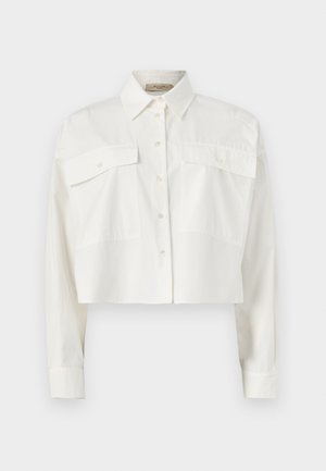 Chemise blanche raccourcie à manches longues avec deux grandes poches avant à rabat et un col pointu sur un fond uni.