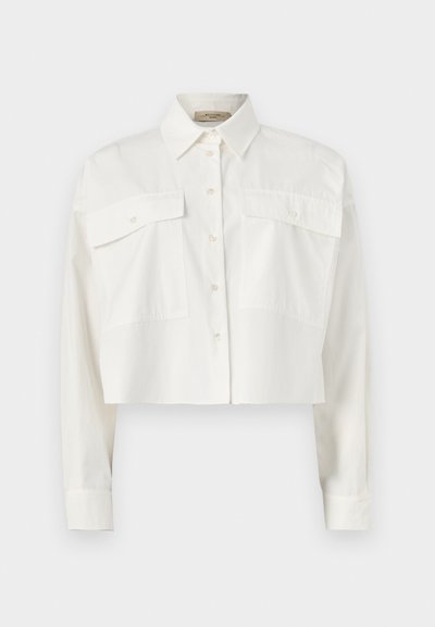 Λευκό κοντό πουκάμισο με μακριά μανίκια και κουμπιά, δύο μεγάλες μπροστινές τσέπες με καπάκια και μυτερό γιακά σε απλό φόντο.