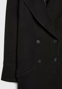 Manteau en laine noir à double boutonnage avec larges revers, quatre boutons et une poche à rabat sur le côté inférieur gauche.