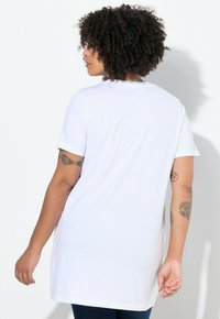 Hvid oversized T-shirt med korte ærmer og rund hals. Har teksten "YOU ARE UNIQUE" i blåt ved bagsiden af halsudskæringen. Glat bomuldsstruktur.