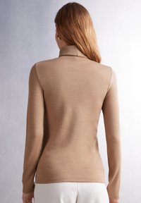 Haut beige à manches longues avec un col montant et une texture côtelée. Tissu lisse, silhouette ajustée, et coutures minimales. Élégance subtile dans le design.