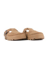 Scarpe slip-on in suede marrone con suola sagomata, caratterizzate da intagli e un accento con fibbia. Superficie testurizzata e suola robusta per una buona aderenza.