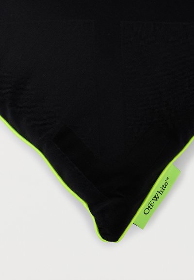 Coussin noir avec bordure vert néon et étiquette de la marque Off-White sur fond blanc.