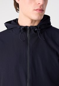 Dark navy hooded jacket featuring a front zipper, adjustable drawstrings on the hood, and a smooth, matte fabric texture.