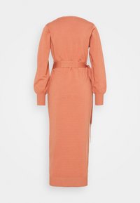 Långärmad, stickad klänning i korall. Har en bältevidd och en rak silhuett. Mjuk textur, med ribbade ärmslut och halsringning.