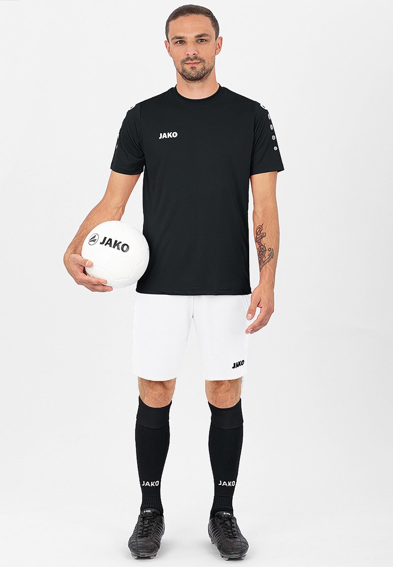 Schwarzes sportliches T-Shirt mit kurzen Ärmeln, weiße Shorts, schwarze Kniestrümpfe und schwarze Fußballschuhe. Hält einen weißen Fußball mit Logo.