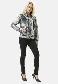 Black and white printed hooded sweatshirt with a zip front, featuring two front pockets and a soft textured fabric. Worn with black jeans.