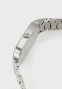 Montre en acier inoxydable avec un fini brossé, boîtier carré et bracelet à maillons métalliques. Dispose d'une couronne ronde sur le côté pour les réglages.
