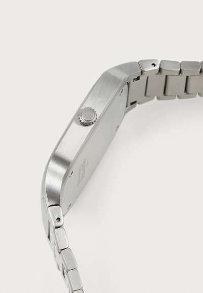 Stainless steel watch with a brushed texture, square case, and metal link strap. Features a round crown on the side for adjustments.