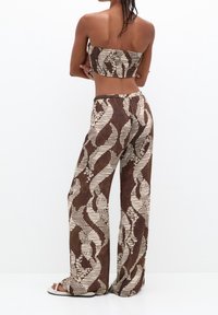 Completo a due pezzi con un motivo marrone e crema. La parte superiore è un crop top senza spalline con un design arricciato, mentre i pantaloni a gamba larga presentano un motivo audace.