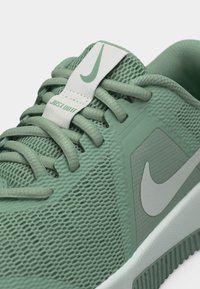 Κοντινό πλάνο ενός πράσινου αθλητικού παπουτσιού Nike με υφή από πλεγμένο δίχτυ, κορδόνια και εμφανή λογότυπα της μάρκας στη γλώσσα και την πλαϊνή πλευρά.