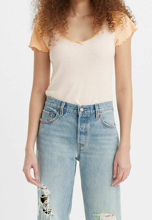 Jasno brzoskwiniowy top z kontrastowymi pomarańczowymi rękawami z falbankami, zestawiony z jasnoniebieskimi, postrzępionymi, wysokim stanem jeansami.