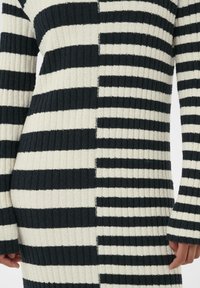 Soonikkoes kleit vahelduvate mustade ja kreemjate horisontaalsete triipudega, mille laius varieerub ja millel on keha järgnev siluett.