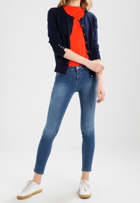 Navy cardigan with buttons, bright orange t-shirt, blue skinny jeans, and white sneakers with a tan sole. Simple, fitted design.