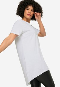 Witte tuniek met korte mouwen en een ronde halslijn, met een langere achterkant, gemaakt van zachte stof. Gecombineerd met zwarte leggings.