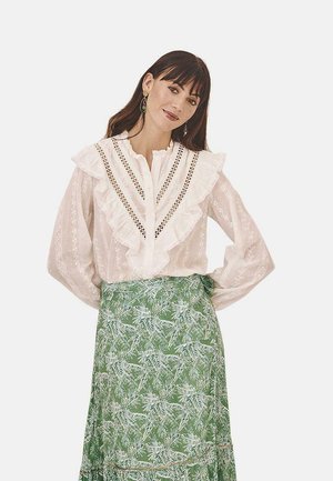 Blusa blanca con volantes, con botones en el frente y detalles de encaje, combinada con una falda verde de estampado floral.
