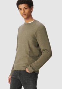 Olivgrüner Rundhalsausschnitt-Sweater mit gerippten Seitenpaneelen und langen Ärmeln, aus weichem Stoff gefertigt. Kombiniert mit dunklen Jeans.